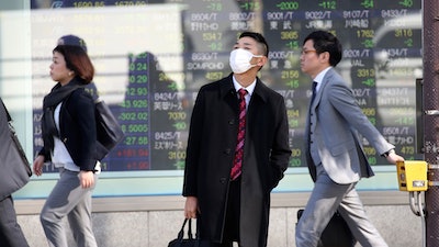 In this Nov. 21 photo, people walk in front of an electronic stock board of a securities firm in Tokyo.