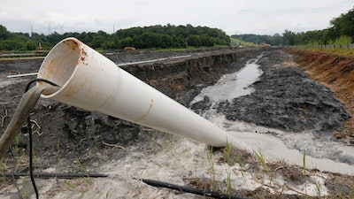 In this June 26, 2015 file photo a drain pipe sticks out of a coal ash retention pond at the Dominion Power's Possum Point Power Station in Dumfries, Va. A new report released Friday, Dec. 1, 2017, from Dominion Energy says it would be cheaper and quicker to close and cover coal ash ponds than to recycle the waste or move it to landfills.